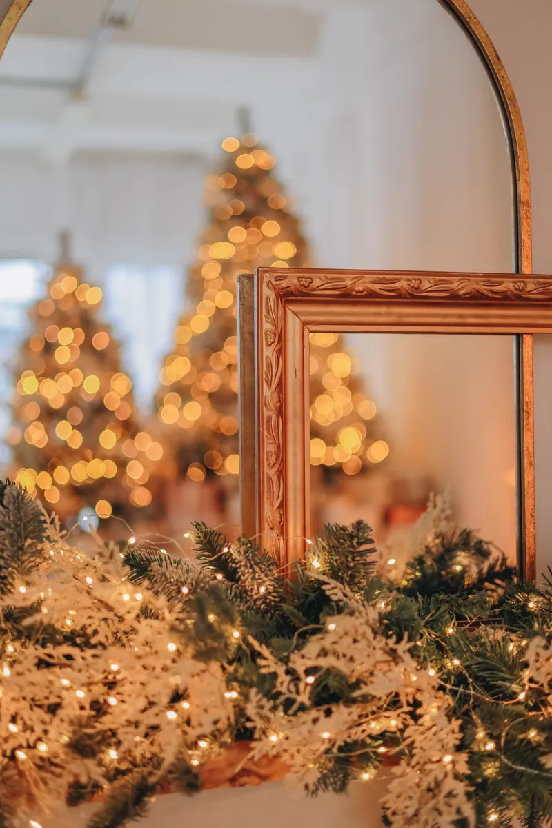 A Small Room, Dressed for December, That Still Works Every Morning 1 Arched mirror with a lit garland and fairy lights, with lit trees reflected in the glass