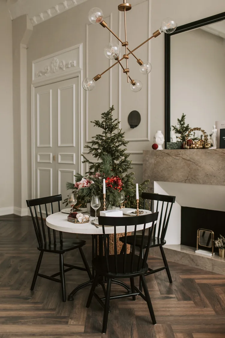 Seven Moves That Turn the Dining Table Into Christmas 4 A modern brass chandelier with globe bulbs over a small round table set for Christmas dinner