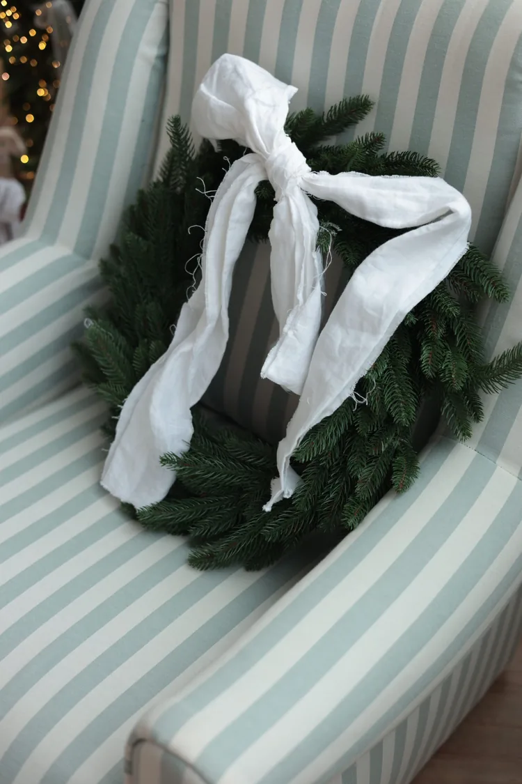 Seven Moves That Turn the Dining Table Into Christmas 5 A green wreath with a white ribbon resting on a striped armchair