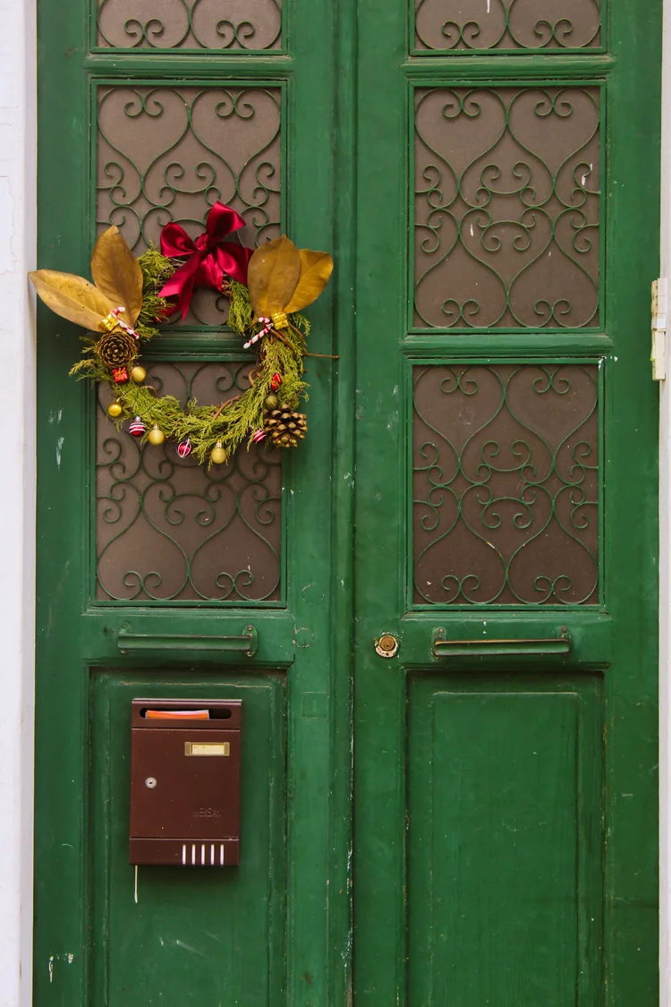 A Christmas wreath with gold leaves and a red bow hanging on a green double door