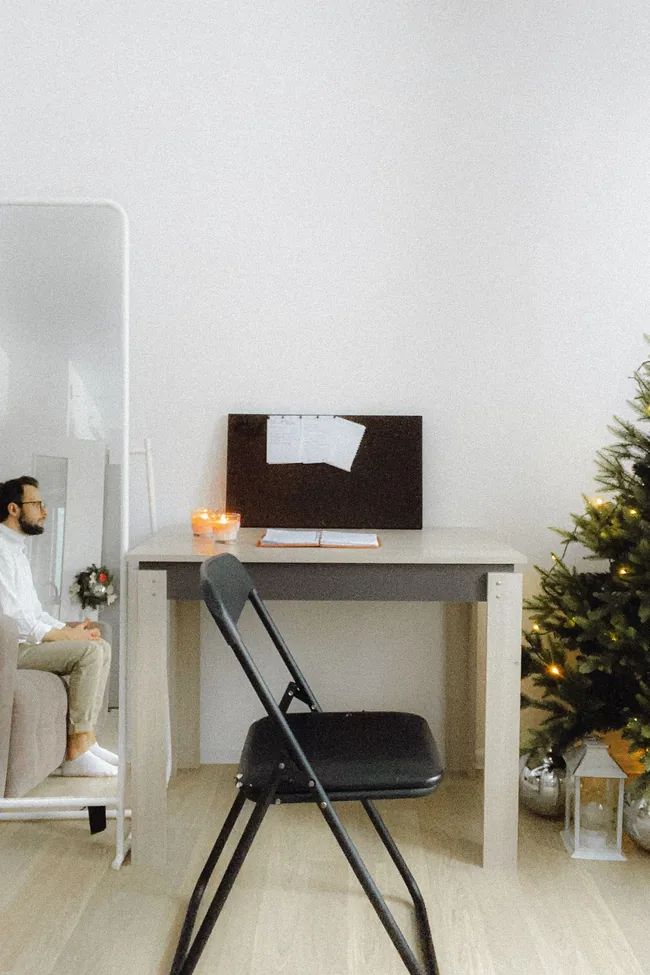 A tidy desk corner with a plain wall and a lit Christmas tree at the edge, a calm video call background