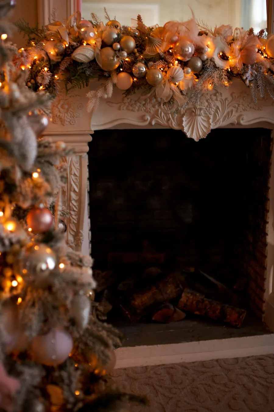A Christmas mantel glowing with warm lights at dusk beside a lit tree