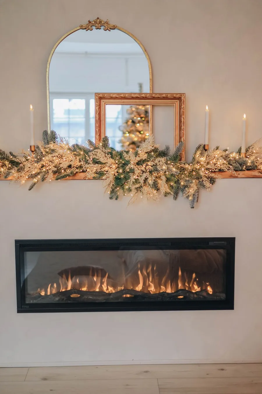 An arched gold mirror above a Christmas mantel with a lit garland