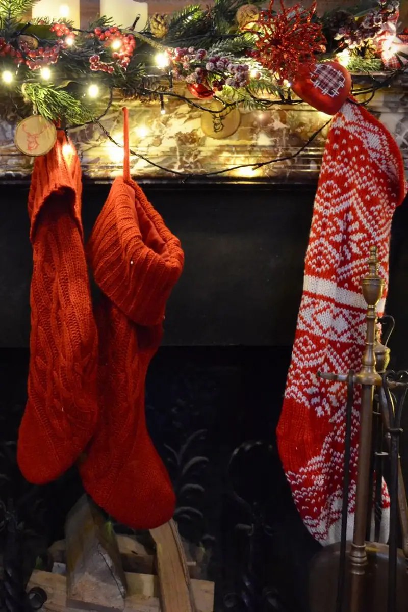 Christmas stockings hung on a fireplace mantel under a lit garland