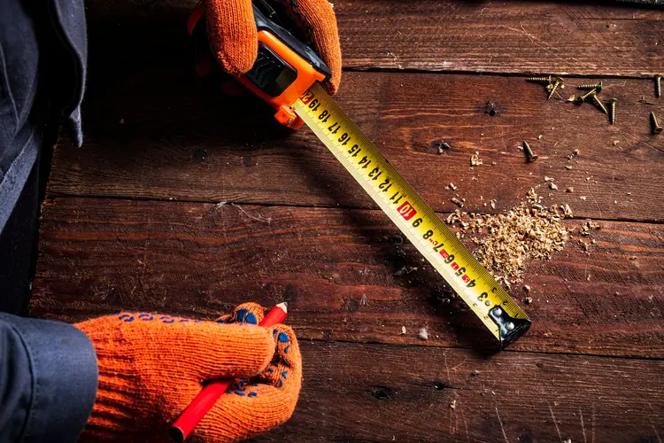 Gloved hands holding a yellow tape measure across a wooden workbench