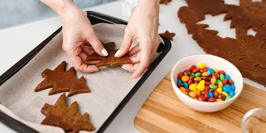 A Warm, Workable Holiday Kitchen: Greenery, Brass and Room to Cook 4 Christmas tree shaped cookies being placed on a baking tray on a kitchen counter.