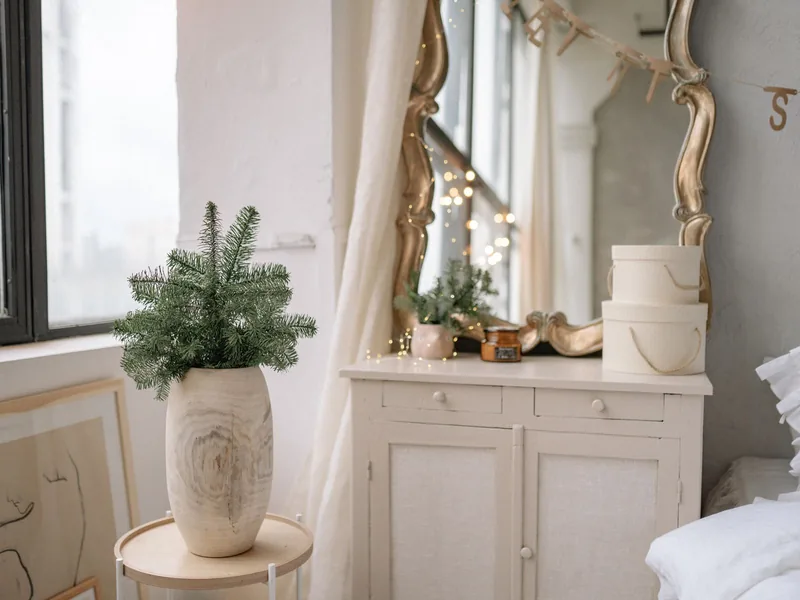 A Calm, Green Holiday Bedroom You Can Actually Sleep In 1 Fir sprigs in a pale vase on a small table beside a white dresser with a gold mirror
