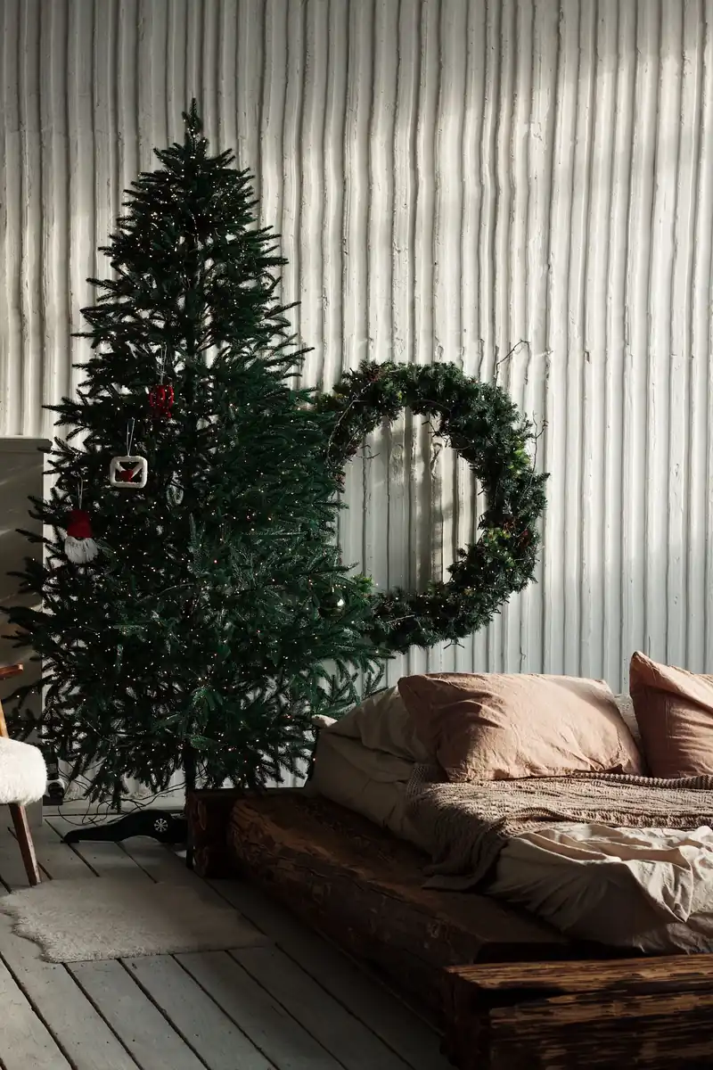 A Calm, Green Holiday Bedroom You Can Actually Sleep In 6 A slim Christmas tree and a large evergreen wreath beside a low wooden bed with neutral bedding