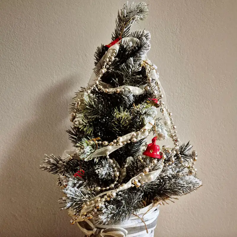 A Calm, Green Holiday Bedroom You Can Actually Sleep In 4 A small frosted tabletop tree with ribbon, bead garlands and a red bell on a wooden table