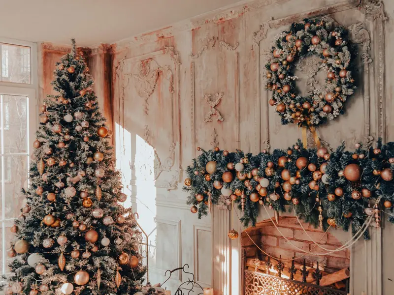 A Calm, Green Holiday Bedroom You Can Actually Sleep In 8 A living room fireplace dressed with an evergreen garland and a large wreath, with a Christmas tree beside it
