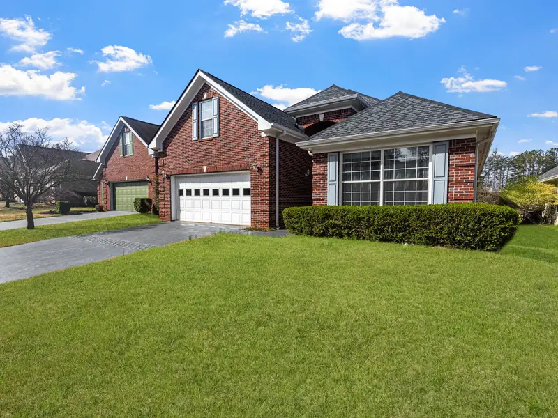 A red brick suburban house with a green lawn and driveway on a bright day, before any Christmas lights go up.