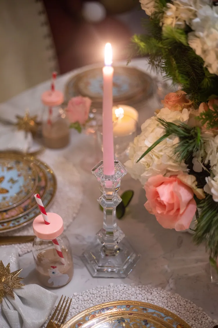7 Ways to Make Pink Feel Like Christmas, Not a Party 5 A dinner table with a lit pink candle, pink roses and ornate plates.
