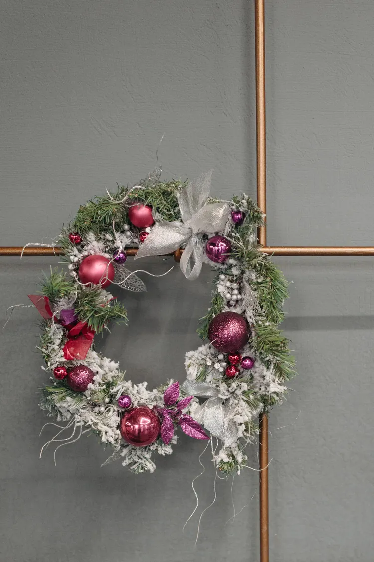 7 Ways to Make Pink Feel Like Christmas, Not a Party 4 A frosted Christmas wreath with pink baubles and a silver bow hanging on a wall.
